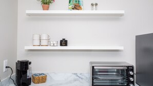 Una cocina con cafetera, horno tostador y repisa con planta en maceta, un libro y un tarro.