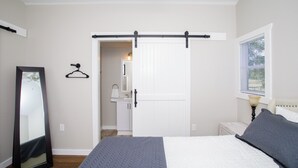 Un dormitorio con una cama, un tocador, un espejo, una puerta y una ventana.
