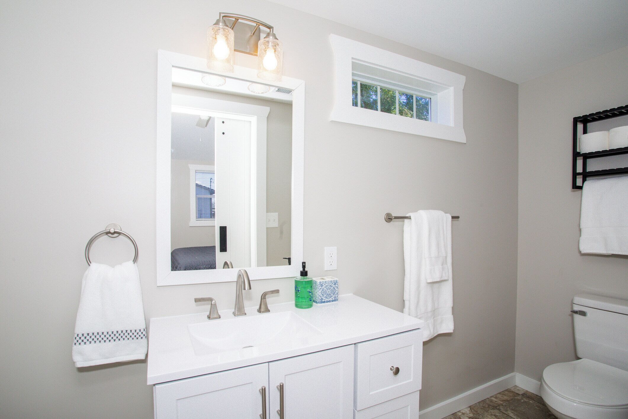 Une salle de bain avec un lavabo blanc, un miroir, une fenêtre et des toilettes.