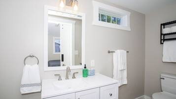 Une salle de bain avec un lavabo blanc, un miroir, une fenêtre et des toilettes.