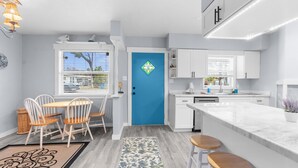 A modern kitchen with white cabinets, a blue door, and a dining area with wooden chairs and a table.