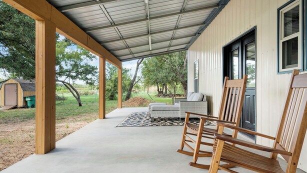 Une véranda avec des chaises en bois, un canapé blanc et un sol en béton.