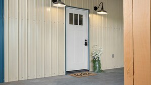 Une porte blanche avec un cadre bleu, un paillasson sur lequel est écrit « bonjour », et deux lampes fixées au mur au-dessus de la porte.