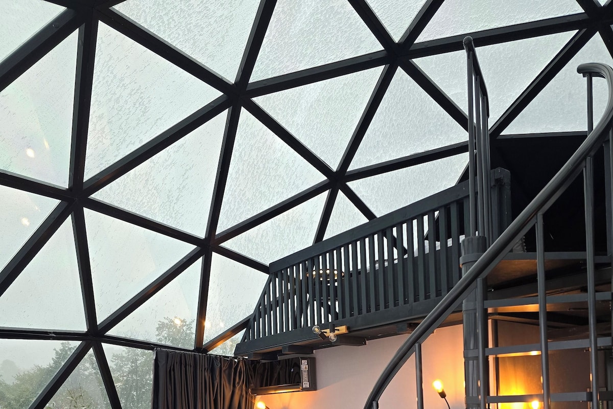 Un interior moderno con techo de vidrio geométrico, un sofá, una mesa y una escalera.