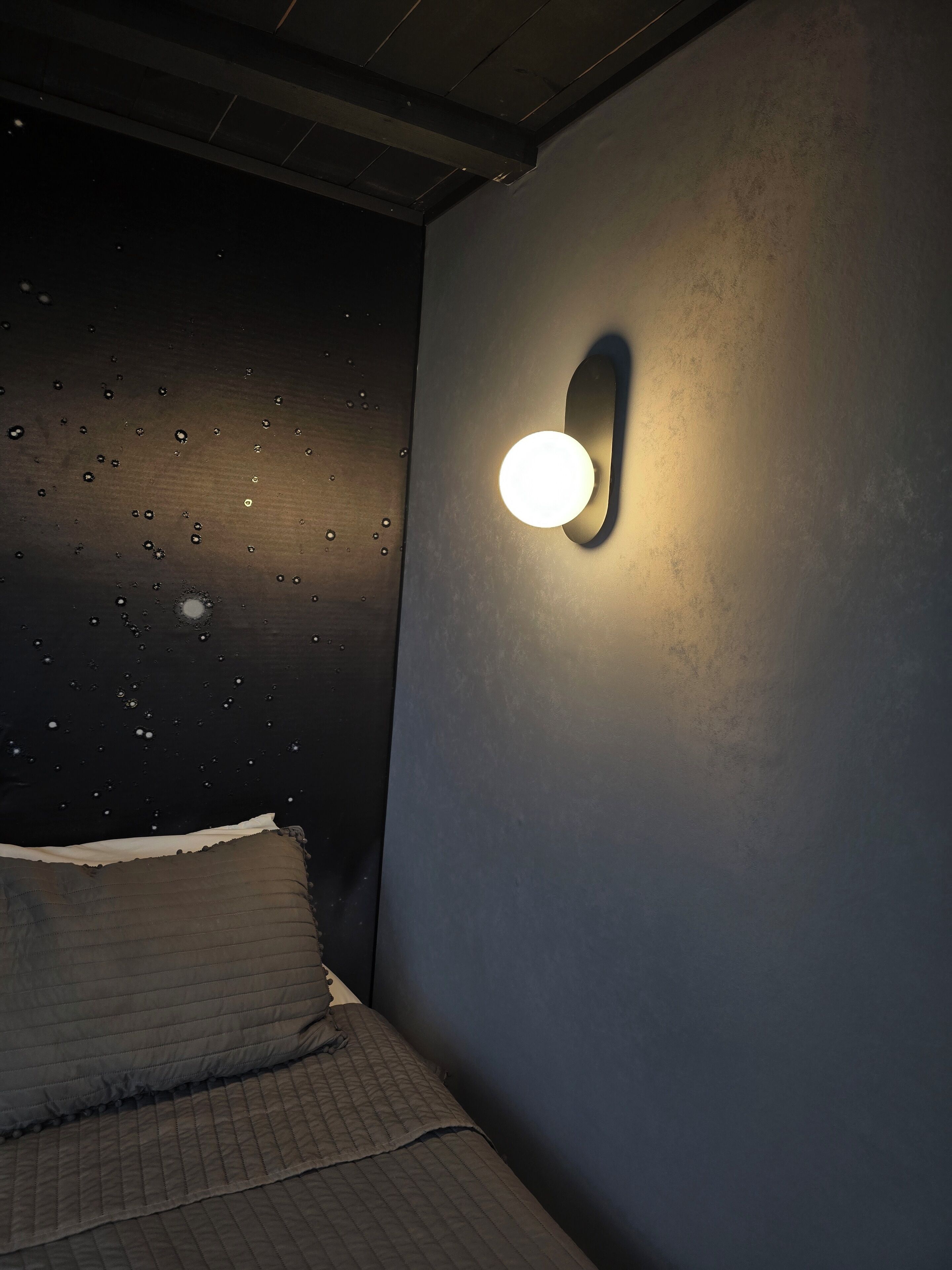 A bedroom with a bed, a wall-mounted light fixture, and a textured wall with water droplets.