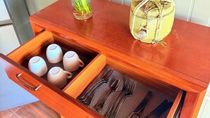 A wooden cabinet with a drawer containing teapots, a woven basket, and a vase with green plants. - Cozy Modern Studio in Maculusso, Luanda – Central & Secure Location (Luanda)