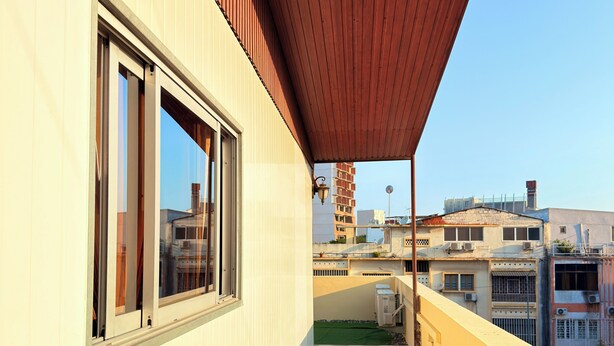A balcony with a wooden floor and a red roof, overlooking a cityscape with buildings and a clear sky. - Cozy Modern Studio in Maculusso, Luanda – Central & Secure Location (Luanda)