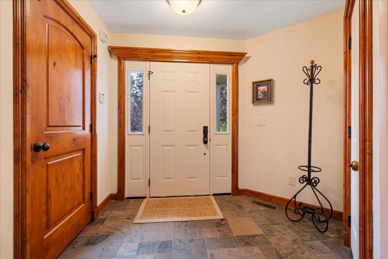 A hallway with a wooden door, a white door, a rug, and a coat rack.