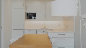 A modern kitchen with white cabinetry, a wooden dining table, and a pendant light. - Montramar (Albufeira)