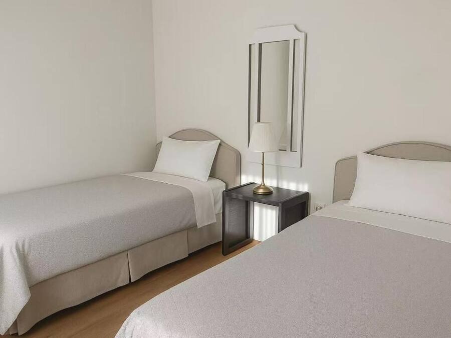 A hotel room with two single beds, a bedside table with a lamp, and a mirror on the wall.