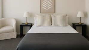A hotel room with a bed, two bedside tables with lamps, a chair, and a framed leaf artwork on the wall. - Cooks Endeavour Motor Inn (Tweed Heads)