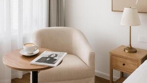 A hotel room with a single armchair, a small round table with a cup and a magazine, a bedside lamp, and a framed artwork on the wall. - Cooks Endeavour Motor Inn (Tweed Heads)