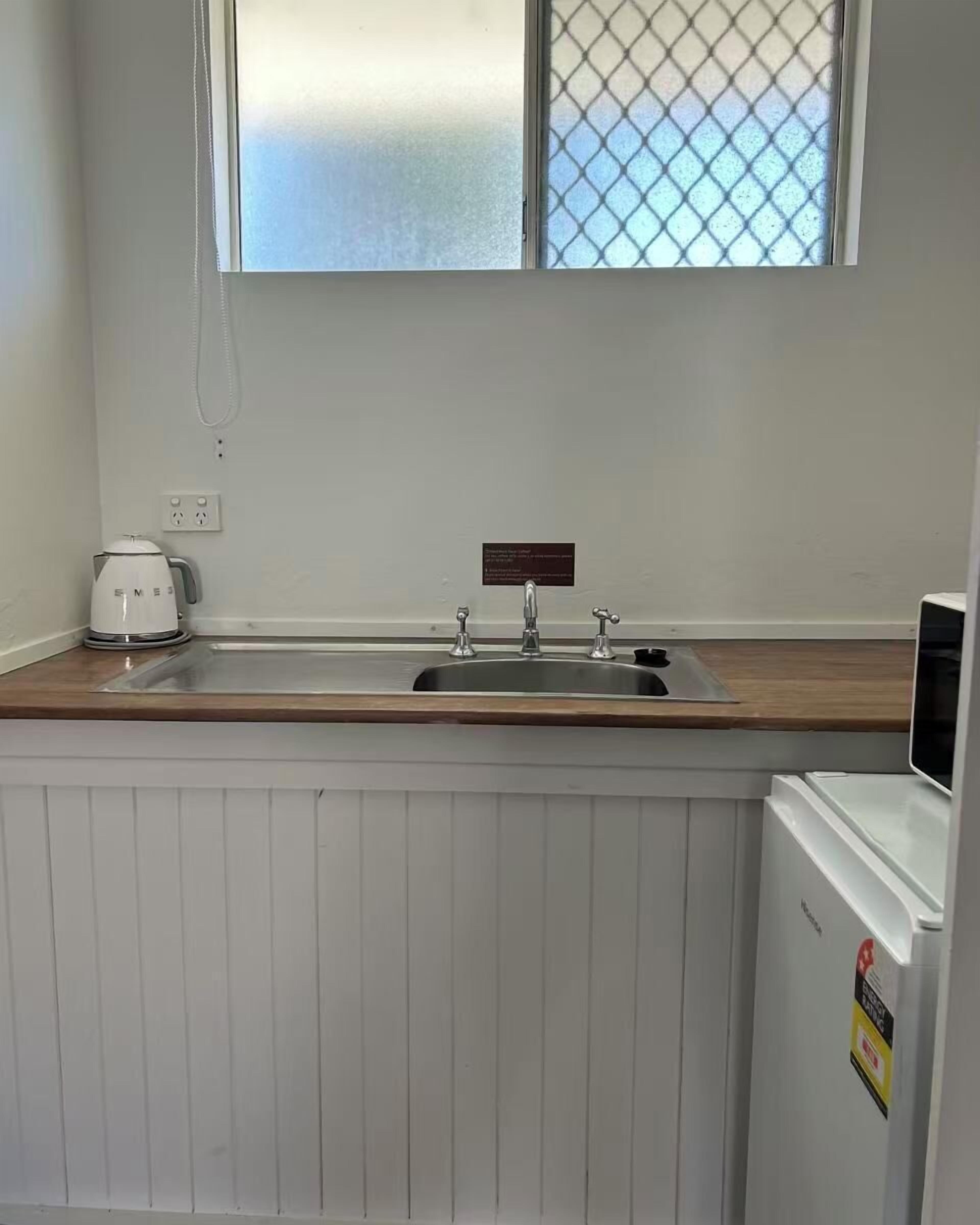A small kitchenette with a white countertop, a sink, a kettle, and a refrigerator.