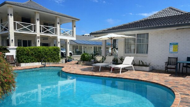 A swimming pool with lounge chairs and a covered patio area. - Cooks Endeavour Motor Inn (Tweed Heads)