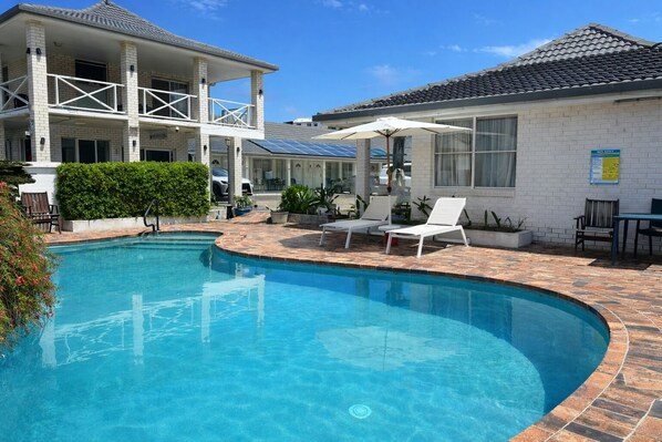A swimming pool with lounge chairs and a covered patio area. - Cooks Endeavour Motor Inn (Tweed Heads)