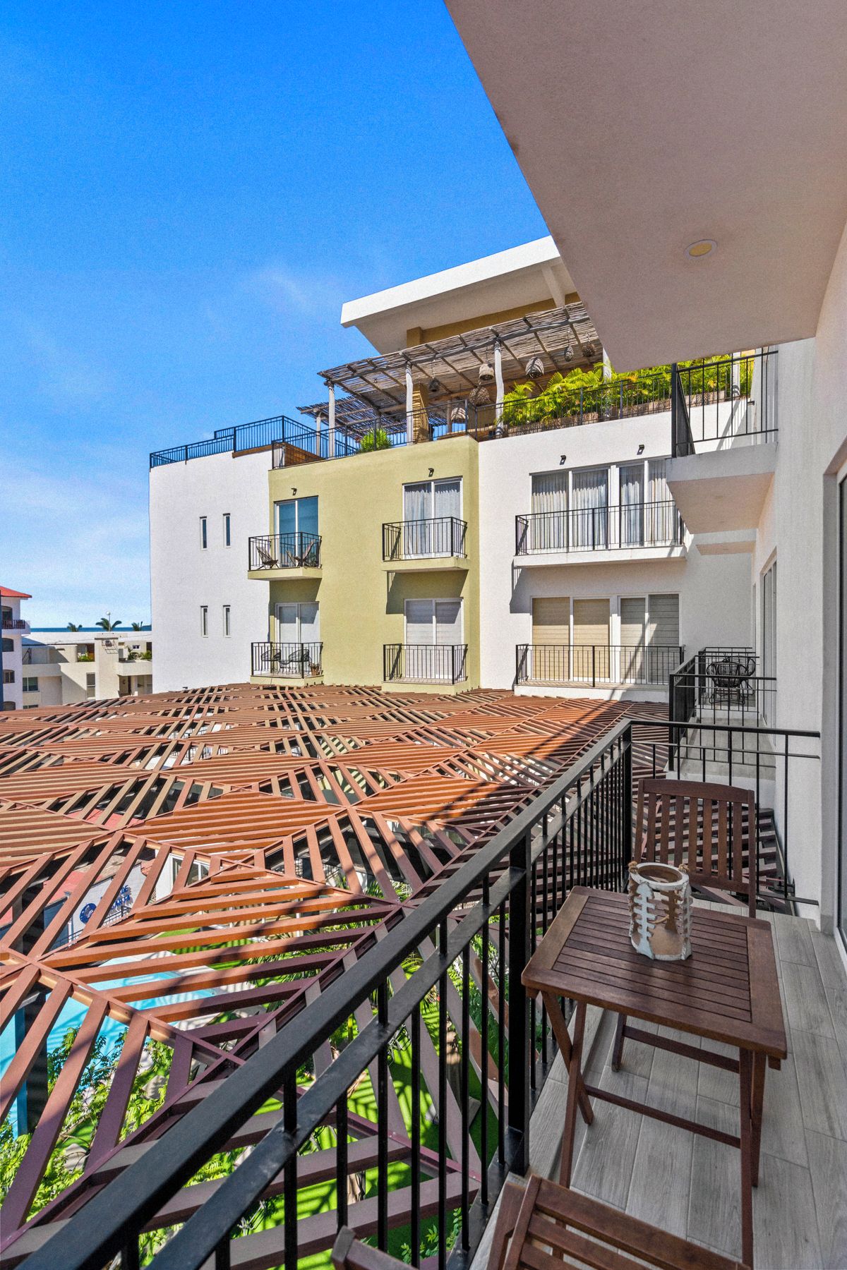 A rooftop terrace with a wooden deck and metal railings, overlooking a residential area with multiple buildings.