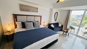 A modern hotel room with a large bed, a ceiling fan, a balcony with a view, and a small seating area. - Life Bucerias Modern Studio Near Beach (Bucerías)