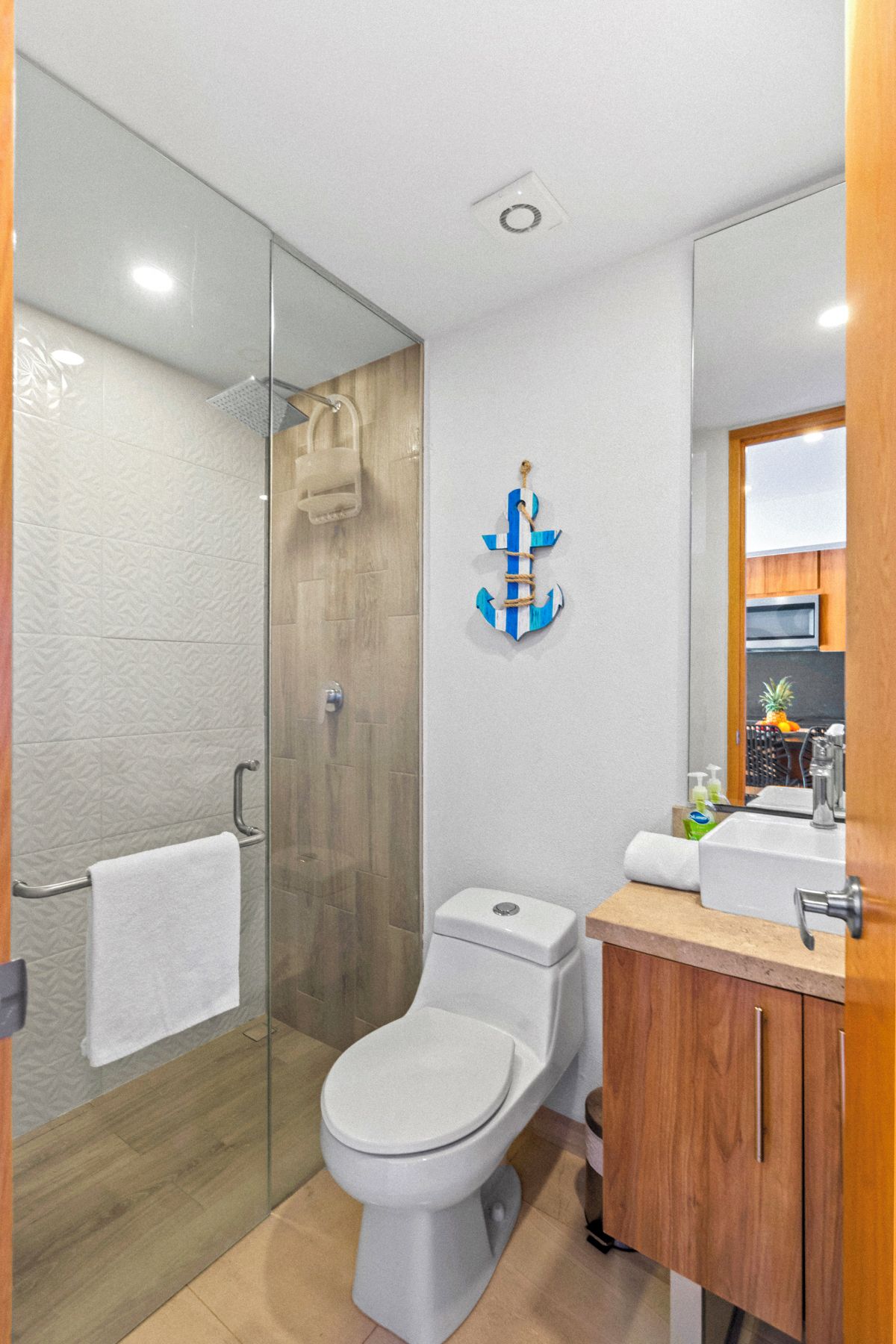 A modern bathroom with a glass shower enclosure, a white toilet, and a wooden vanity with a mirror.