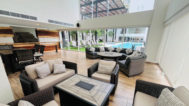 A spacious outdoor lounge area with wicker furniture, a pool, and a view of the surrounding buildings. - Life Bucerias Modern Studio Near Beach (Bucerías)