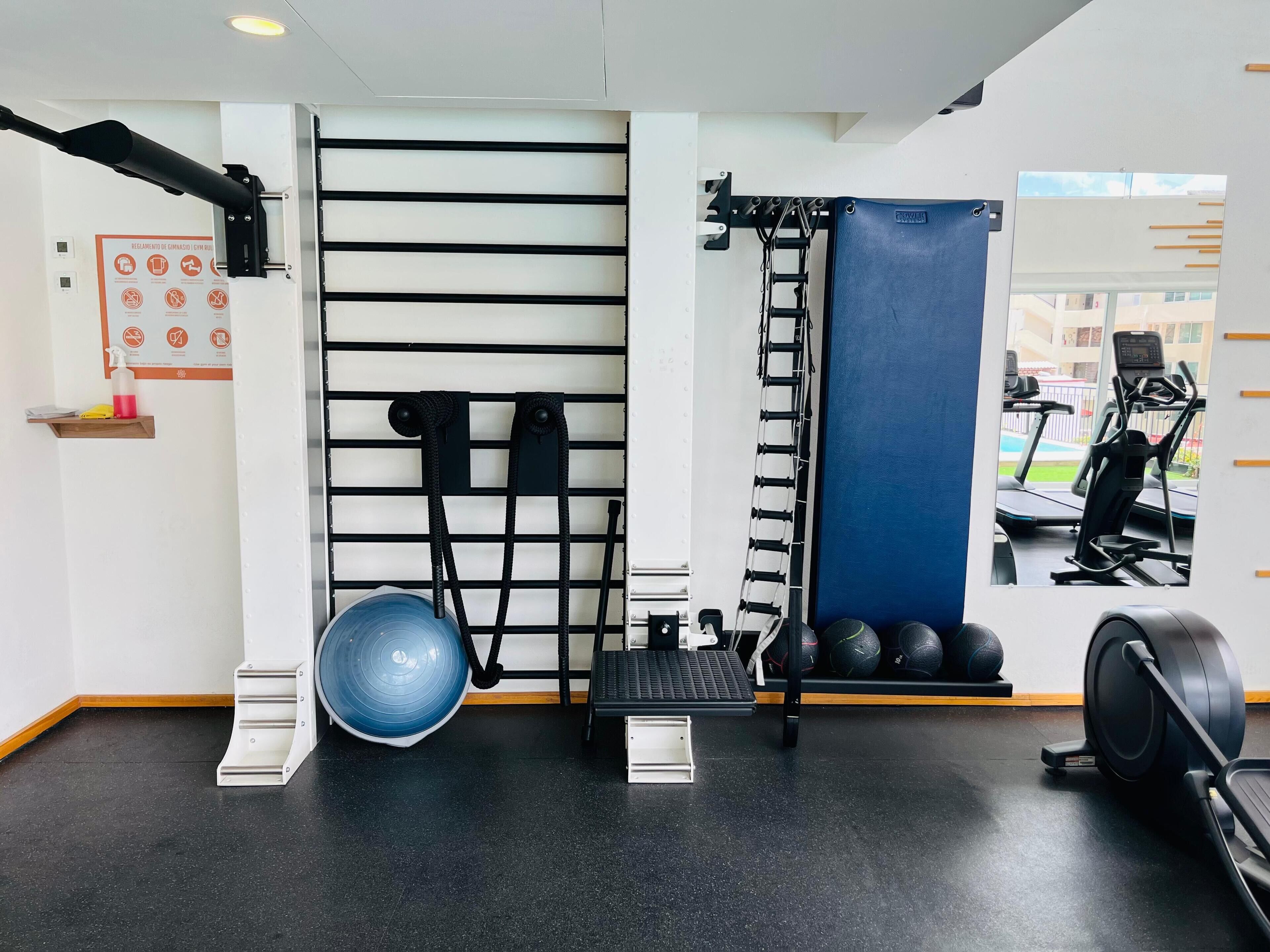 Een sportschool met trainingsapparatuur, een spiegel en een raam met uitzicht op buiten.
