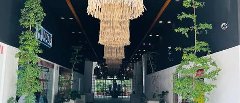A modern interior with a hanging woven light fixture, potted plants, and a visible entrance to a building with signage.