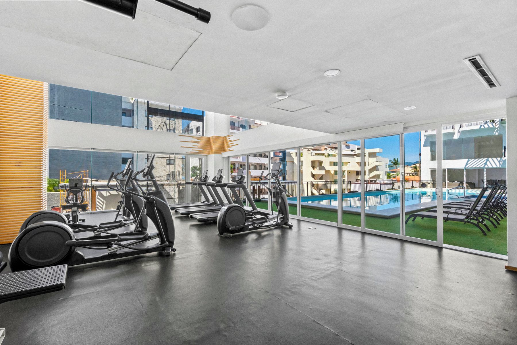 A gym with treadmills, stationary bikes, and weight machines, overlooking a pool and buildings.