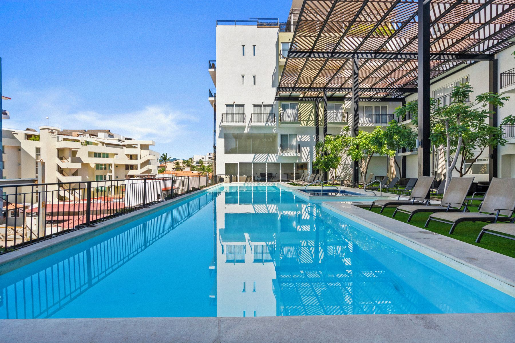 A swimming pool with lounge chairs and a covered seating area, surrounded by buildings.