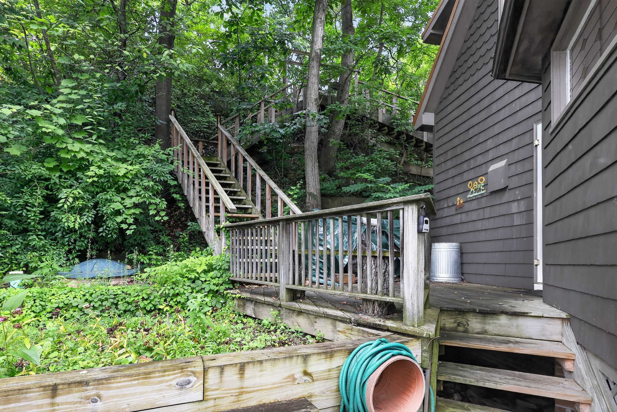 Un escalier en bois mène à une maison entourée d’une végétation luxuriante.