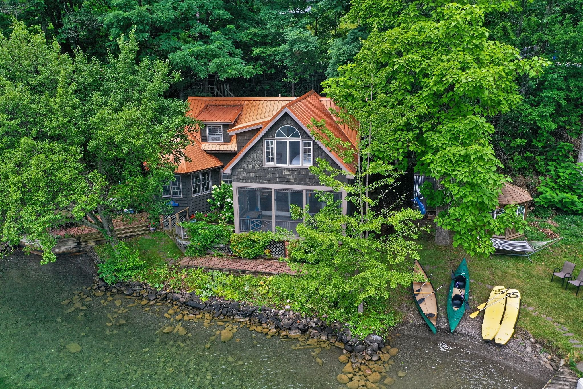 Ein Haus mit einer Stein-Fassade, einer Holzterrasse und einem Teich.