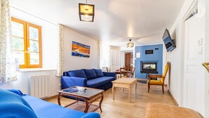 Ett vardagsrum med en blå soffa, ett träbord och en gul fåtölj. Det finns en tavla på väggen och en tv som är monterad på väggen.