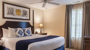 A hotel room with a large bed, a ceiling fan, a nightstand with a lamp, and a window with curtains.