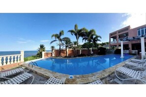 A pool area with lounge chairs, palm trees, and a view of the ocean. - Exotic Paradise Guest House  (Yabucoa)