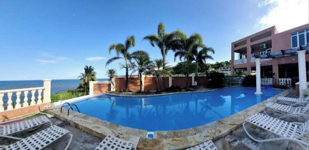 A pool area with lounge chairs, palm trees, and a view of the ocean.