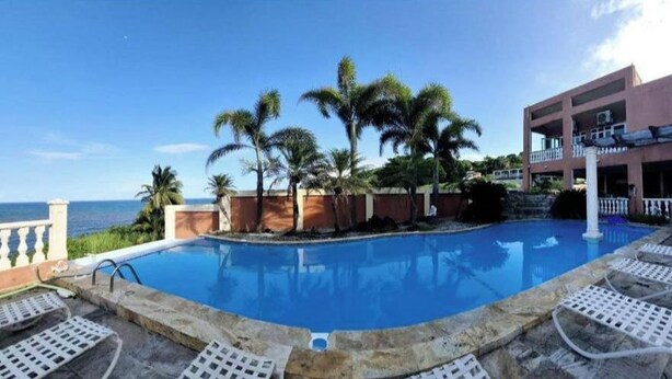 A pool area with lounge chairs, palm trees, and a view of the ocean. - Exotic Paradise Guest House  (Yabucoa)