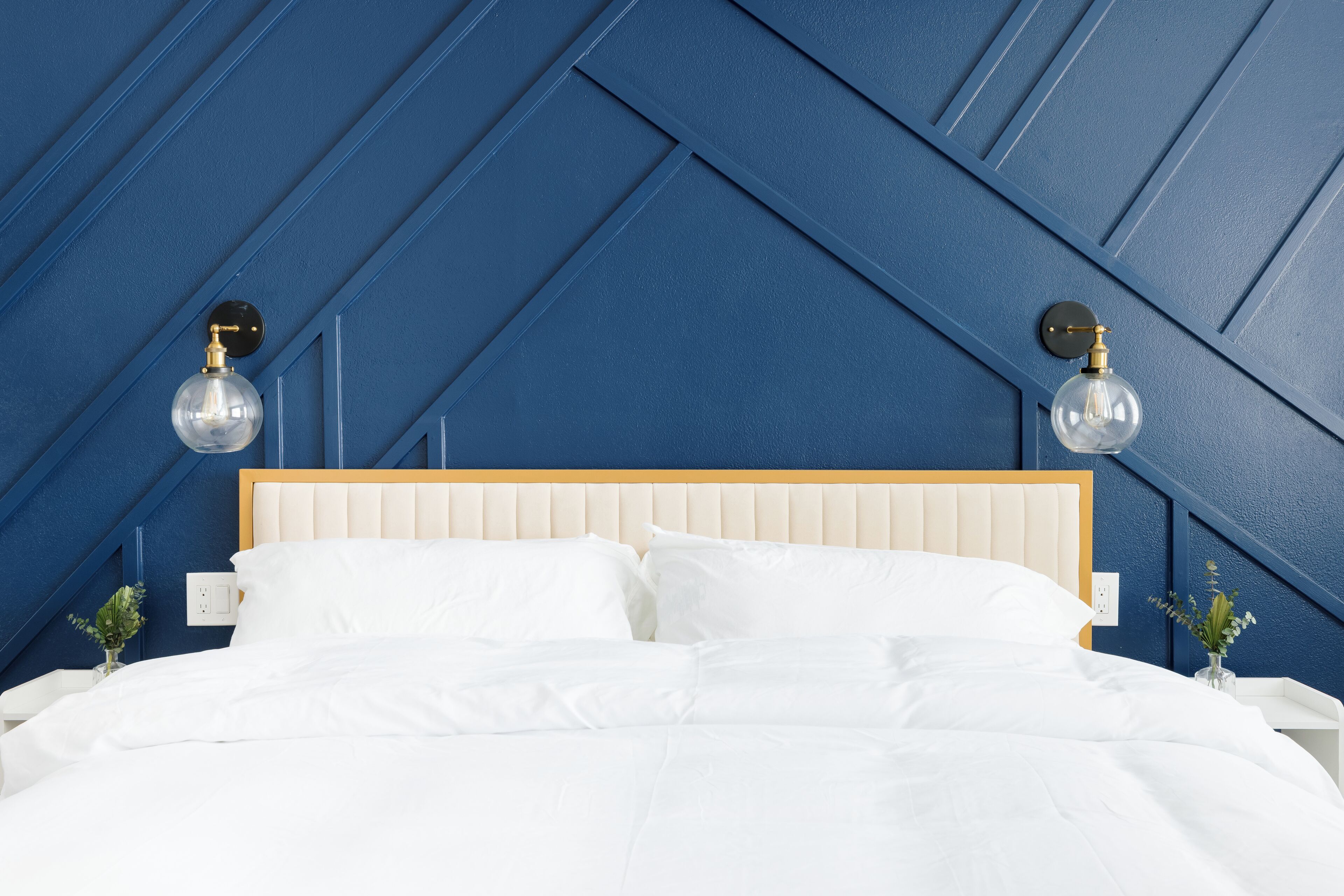 Une chambre à coucher avec un lit, du linge de lit blanc, une tête de lit en bois et deux appliques murales.
