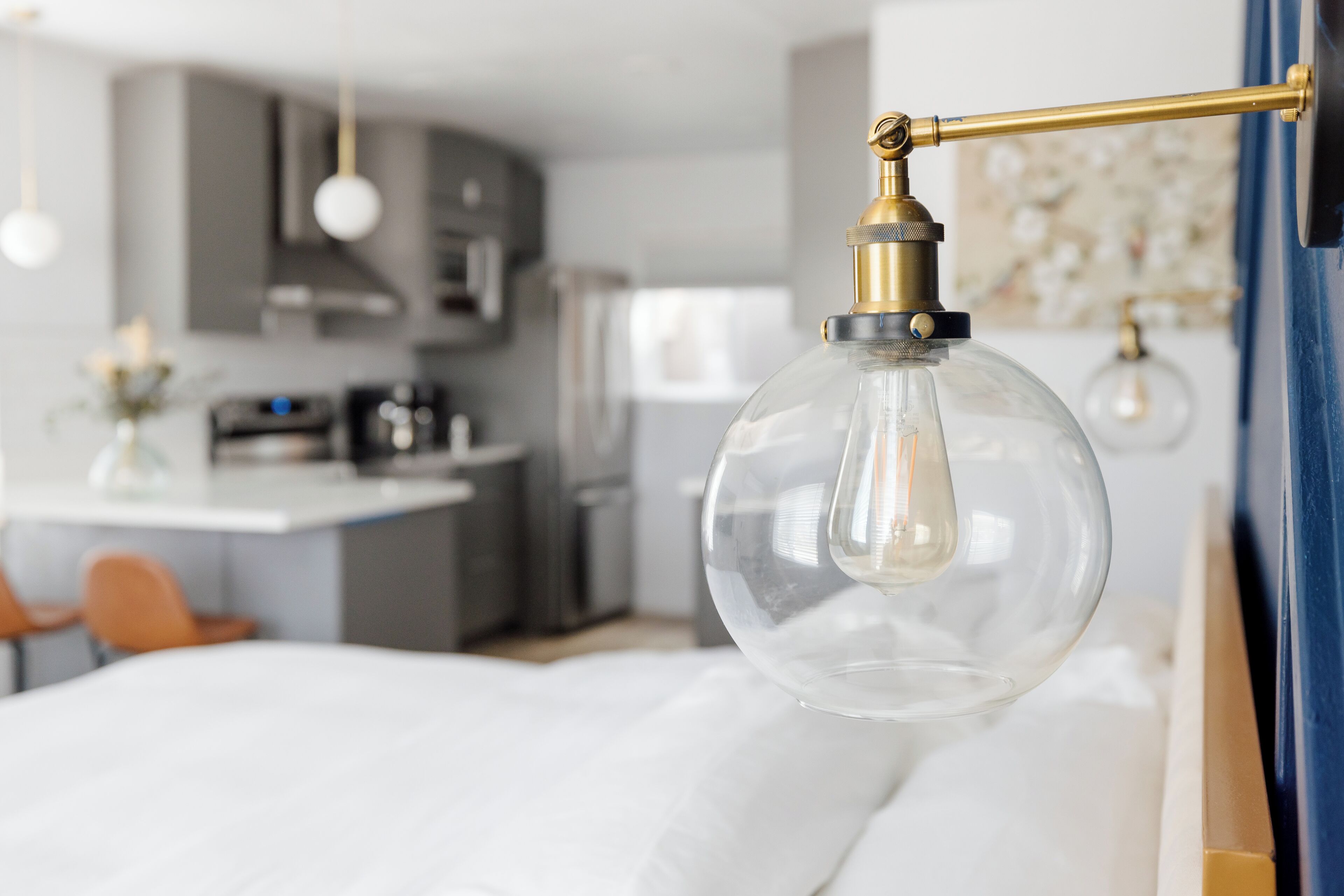Une chambre moderne avec un grand lit, un luminaire suspendu et une vue sur la cuisine et le salon.