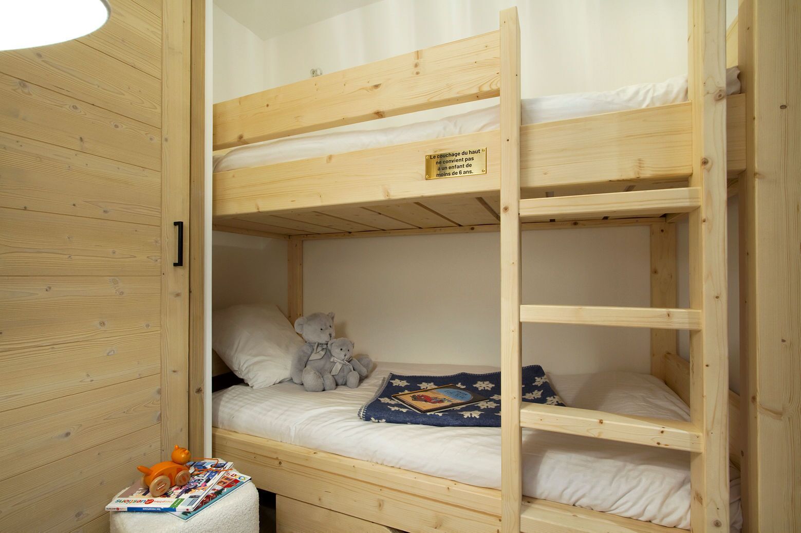 A bunk bed room with a wooden interior, a teddy bear on the lower bunk, and a pillow.