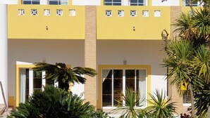 A building with a yellow facade, large windows, and a well-maintained garden with various plants. - Cvl Club House (Lagos)