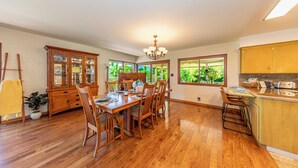 Une cuisine spacieuse avec des meubles en bois, une table à manger et des chaises. Une grande fenêtre offre une vue sur la verdure environnante.