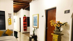 A hotel hallway with a sofa, a small table with a plant, a framed picture, a fire extinguisher, and a door. - Hotel Palma Sevilla Medellin (Medellín)
