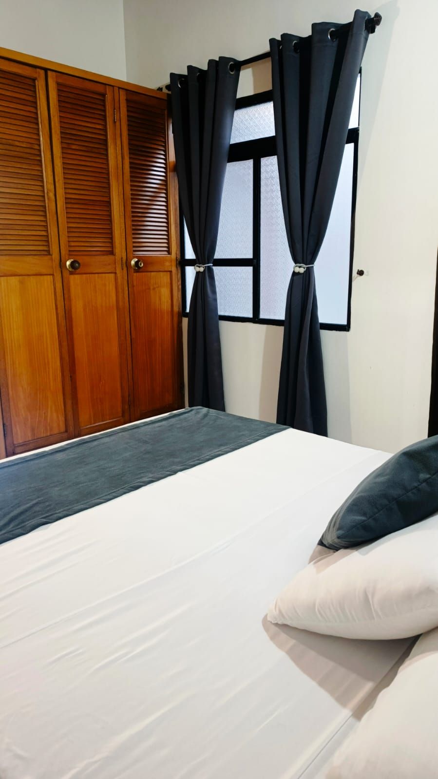A bedroom with a bed, a wooden wardrobe, and black curtains.
