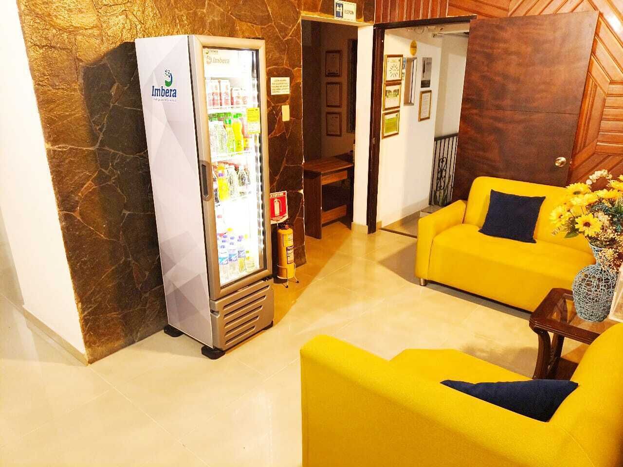 Un hall d’hôtel avec un mini-bar, un canapé jaune et un vase décoratif.