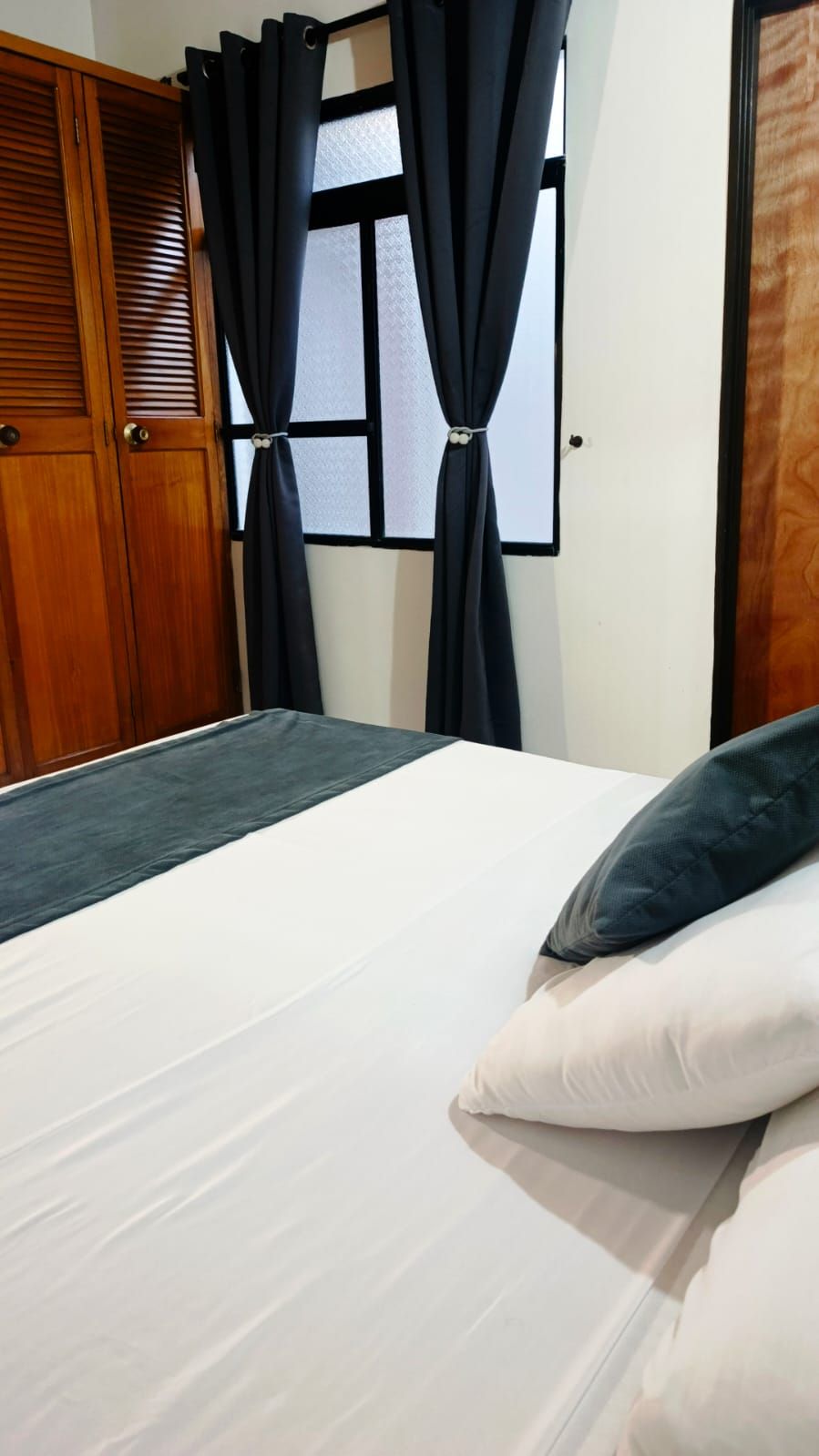 Un dormitorio con cama, un armario de madera y una ventana con cortinas.