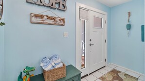 A hallway with a light blue wall, a wooden sign that reads "HOPE", a wicker basket with towels, and a small dinosaur toy.