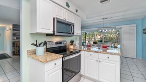 A kitchen with white cabinets, a stainless steel microwave, a stove, and a granite countertop.