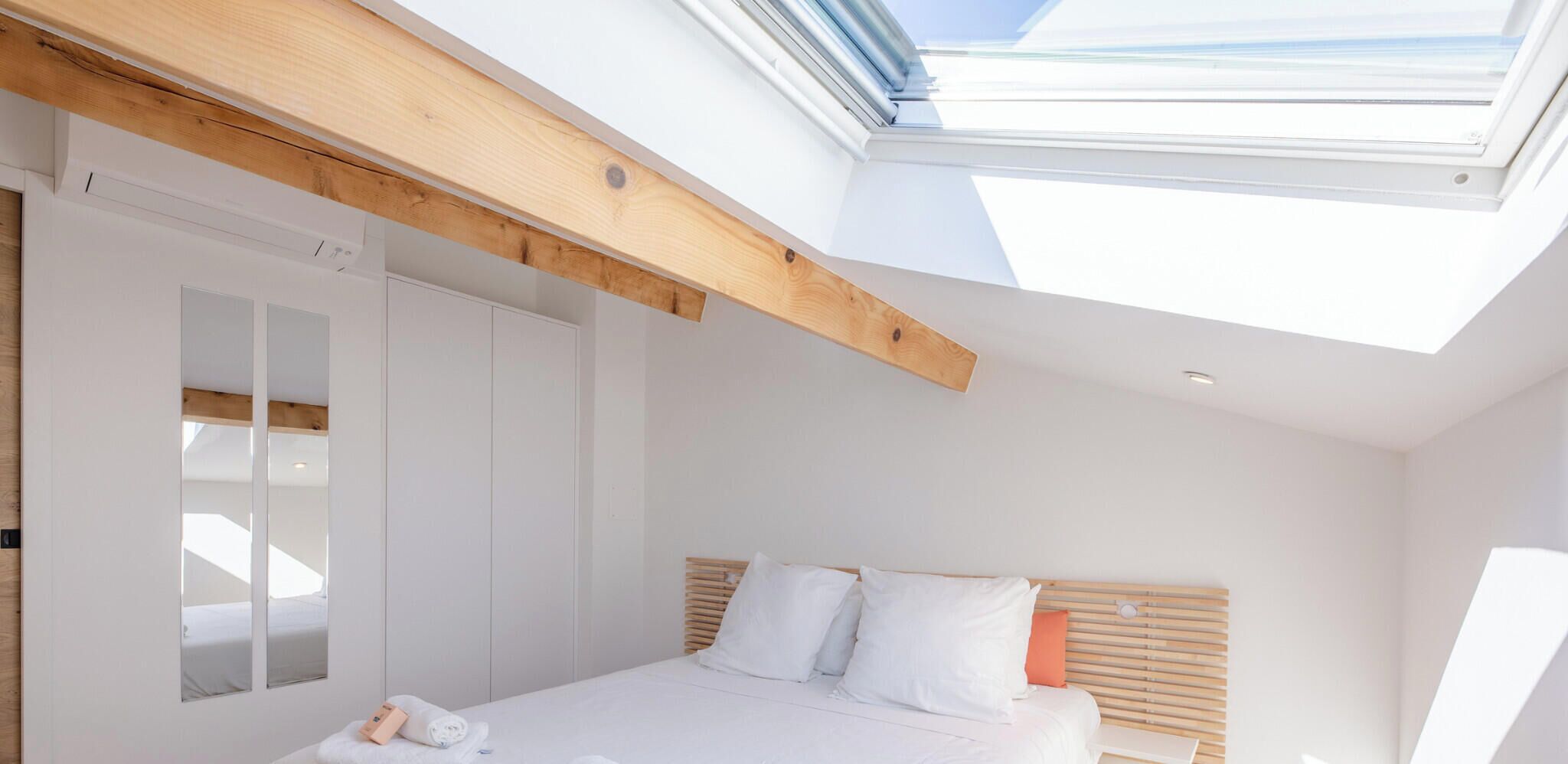 A bedroom with a skylight, a bed with white bedding, and a wooden headboard.