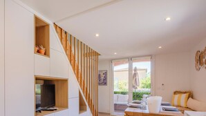 Una sala de estar moderna con una escalera, un comedor con una mesa dispuesta para dos personas, y un gran ventanal con vistas al exterior.