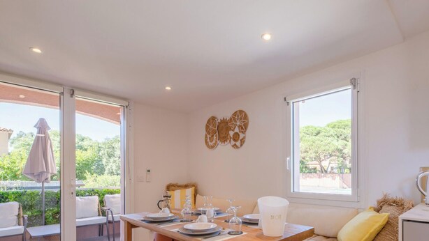 Un comedor con una mesa lista para dos, un televisor en la pared y vistas a zonas verdes.