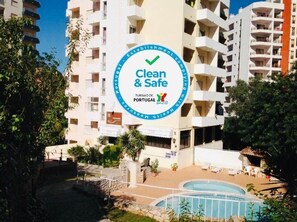 A hotel with a 'Clean & Safe' sign, a swimming pool, and a view of the surrounding buildings.