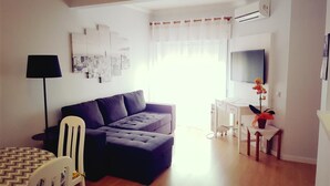 Ein modernes Wohnzimmer mit einer Couch, einem Esstisch, einer Lampe und einem Fernseher.